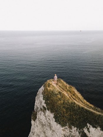 man standing on cliff near body of water