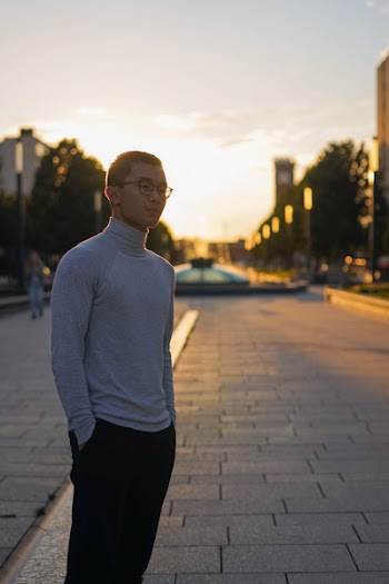 Man Standing on Concrete Road Overlooking Fountain Under Cloudy Sky
