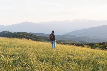 man standing on grass field in mountain
