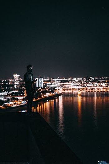 man standing on ledge in front of body of water
