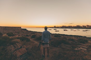 Man Standing on Pathway Near Rocks and Body of Water
