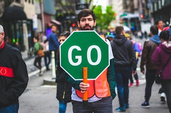 Man Standing on Road Holding Green Go Sign