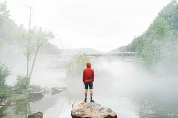 man standing on rock facing foggy creek