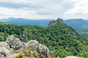 Man Standing on Rock Formation Facing Mountain