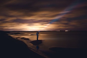 man standing on rock near body of water during golden hour