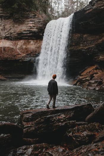 man standing on stone facing waterfalls