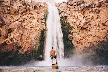 man standing on stone in front of waterfall