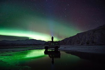 man standing on SUV watching northern lights