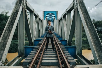 Man Standing on Train Tracks on Bridge Above Body of Water