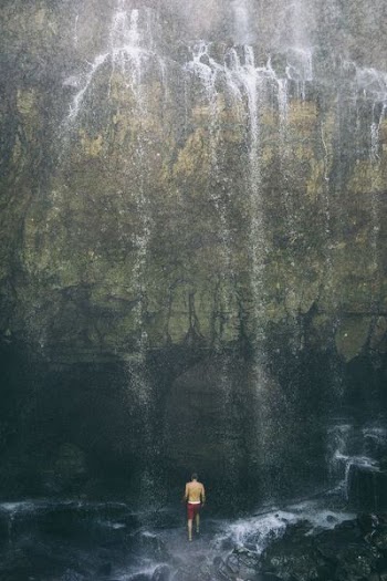 man standing underneath waterfall