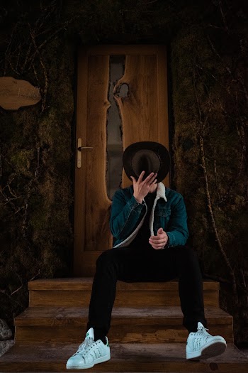 Man Taking Off Cowboy Hat While Sitting On Stairs In Front Of Brown Wooden Door