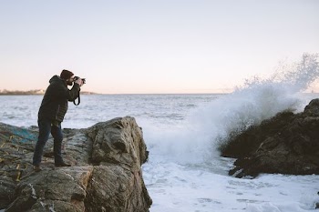 man taking photo of rock formation with sea waves at daytime