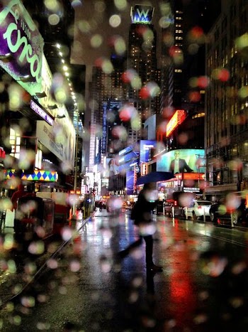 man under blue umbrella walking on road across buildings