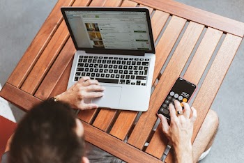 Man Using Laptop and Using Calculator on Phone