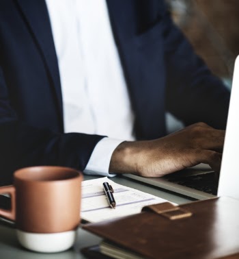Man Using Laptop Beside Mug on Top of Gray Desk