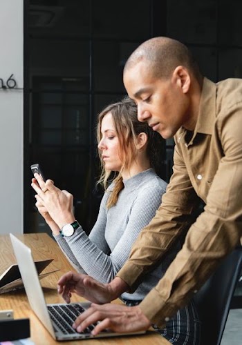 man using laptop besides woman sitting while using smartphone