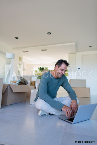 Man using laptop on floor with moving boxes in new house