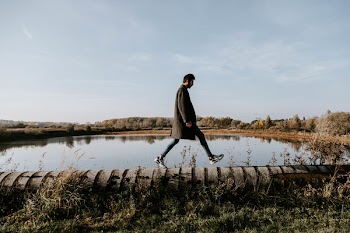 Man Walking on Concrete Pavement Near Body of Water