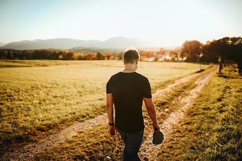 Man Walking on Road Holding Gray Cap