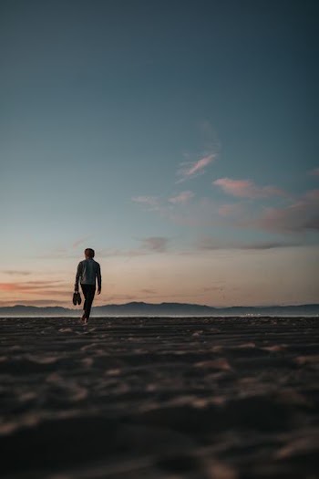 man walking on sand while holding his footwears