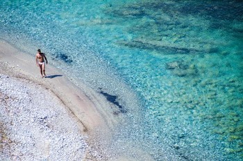 man walking on seashore beside blue se