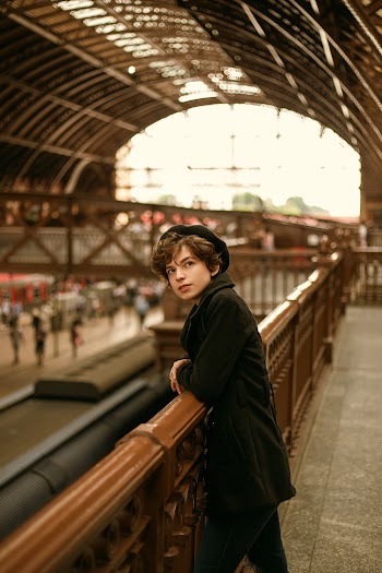 Man wearing a black coat leaning on Brown railing
