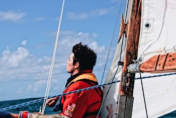 Man Wearing A Life Vest Sitting On A Watercraft Close To The Sail
