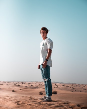 Man wearing a white t-shirt and blue denim pants standing on sand
