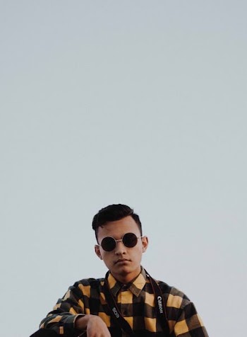 man wearing black and brown button-up collared shirt and black framed sunglasses with Canon lanyard