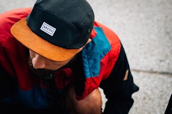 man wearing black and orange Baxin cap looking down