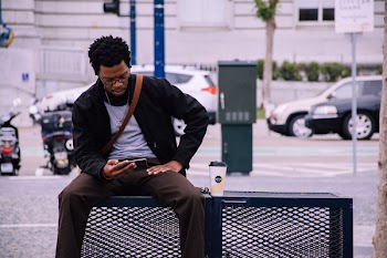 Man Wearing Black Bomber Jacket And Holding Smartphone