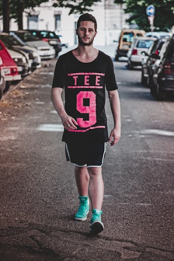 Man Wearing Black Crew-neck T-shirt, Black Shorts, and Pair of Teal High-top Sneakers Walking Between Vehicles