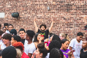 Man Wearing Black Crew-neck T-shirt Raising Hands Near Wall