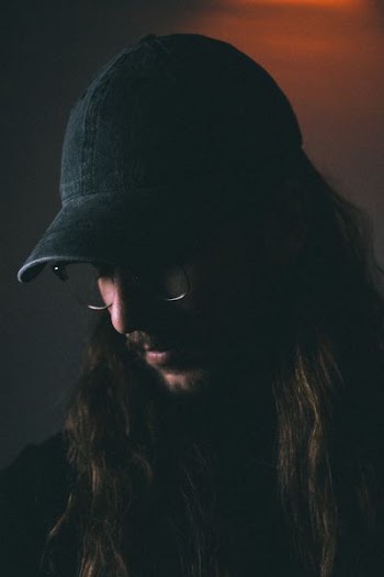 man wearing black fitted cap looking down closeup photography