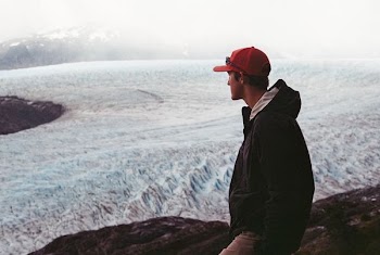 man wearing black hooded jacket on cliff