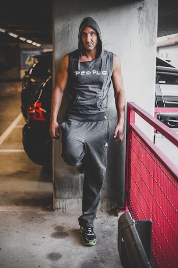 Man Wearing Black Hooded Top and Black Adidas Pants Leaning on Gray Wall