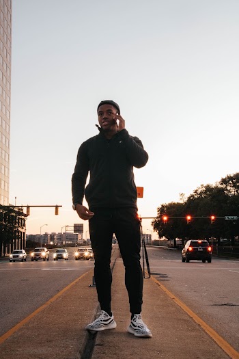 Man Wearing Black Jacket and Black Track Pants Using Smartphone