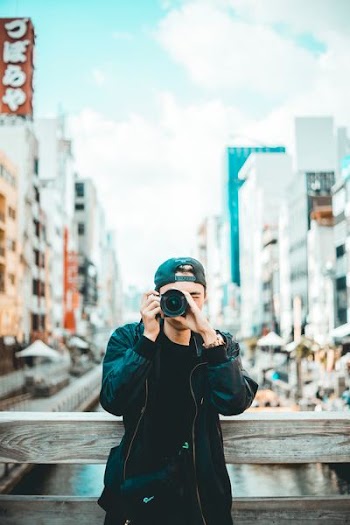 man wearing black jacket and cap holding DSLR camera during daytime