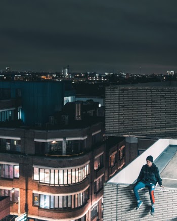 Man Wearing Black Jacket Sitting On Building Rooftop At Nighttime