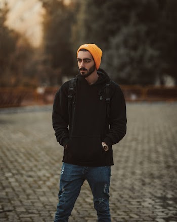 Man Wearing Black Pullover Hoodie, Orange Knit Cap, and Blue Denim Jeans