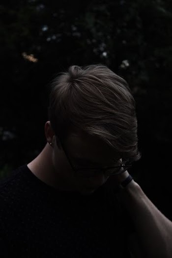 man wearing black shirt and eyeglasses with left hand on neck