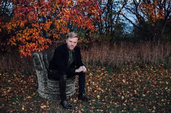 man wearing black suit sits on black concrete chair beside brown tree