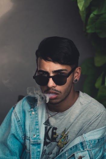 Man wearing black sunglasses and blue denim jacket smoking