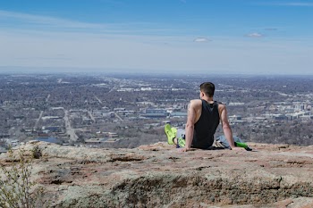 Man Wearing Black Tank Top Sitting Near Edge of Cliff