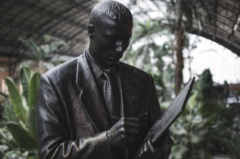 Man Wearing Blazer Holding Book and Pen Statue