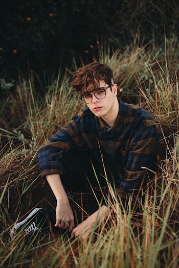 Man Wearing Blue and Brown Plaid Sport Shirt sitting down on grass