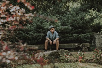 Man Wearing Blue Collared Button-up Long Sleeved Shirt Sitting On Concrete Bench Surrounded With Plants