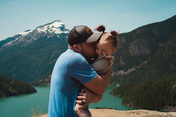 Man Wearing Blue Crew-neck T-shirt Holding Girl Near Mountains