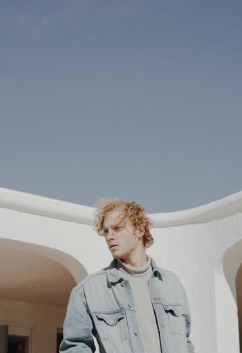 man wearing blue denim jacket near concrete house