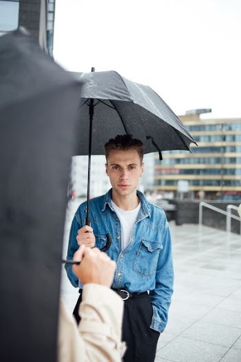 man wearing blue denim stonewashed jacket holding black umbrella
